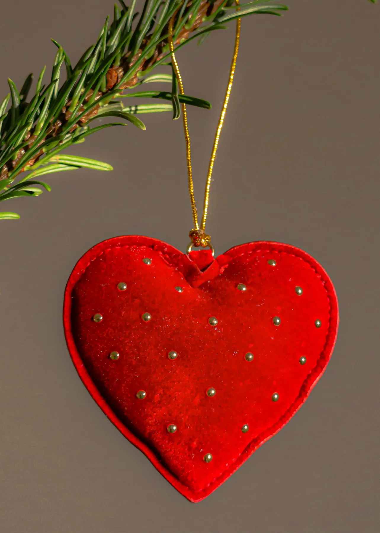 Christmas decoration with red velvet heart ornament suspended from pine branch, symbolizing love and festivity.