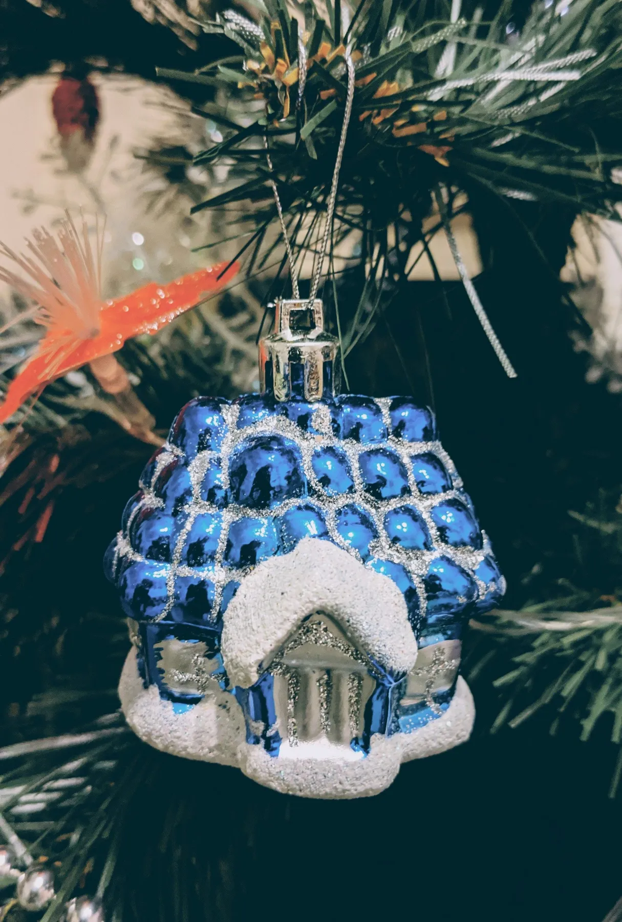 Close-up of a blue house-shaped ornament hanging on a Christmas tree branch.