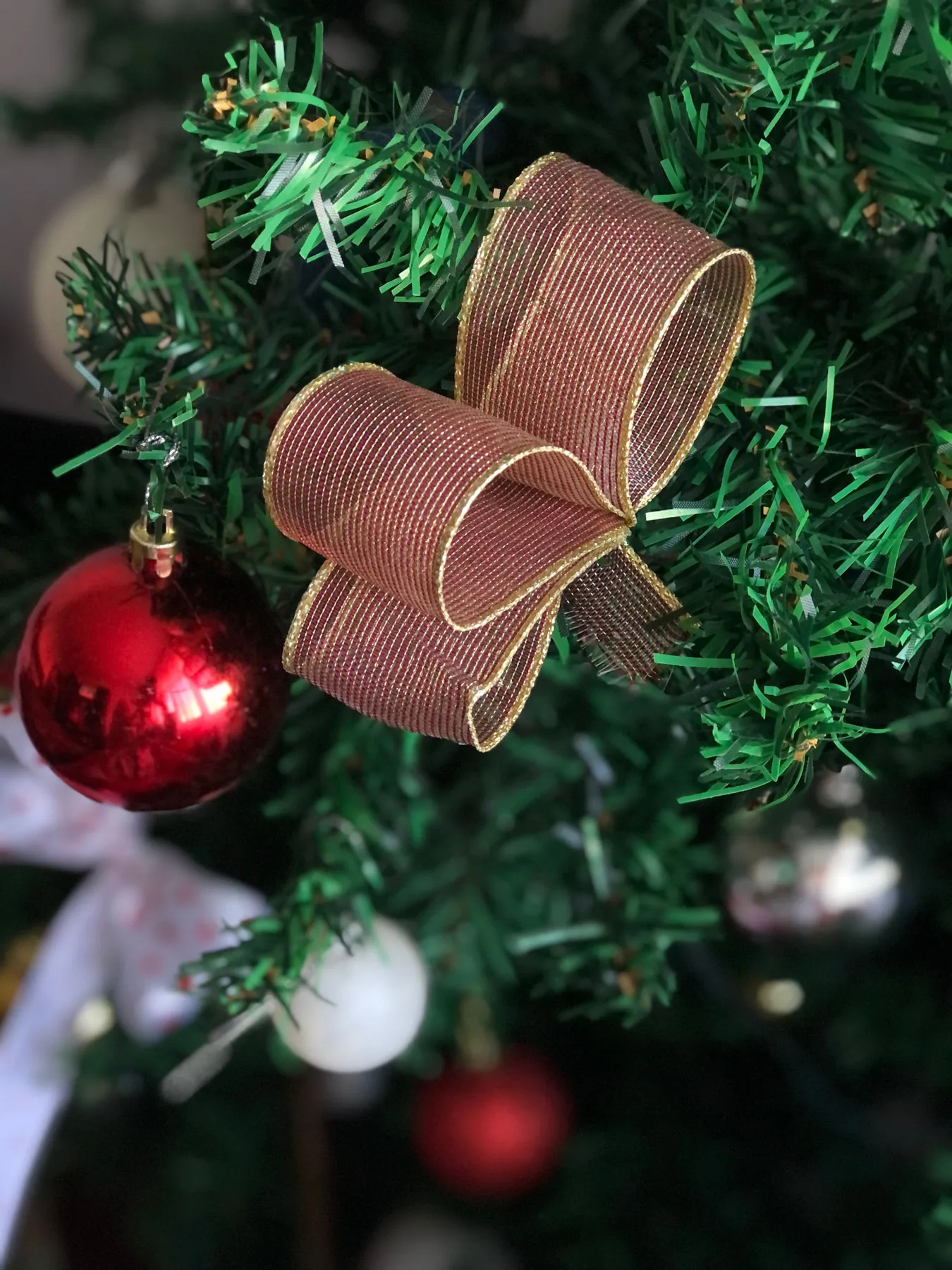 Close-up of a Christmas tree with red ornament and ribbon bow.