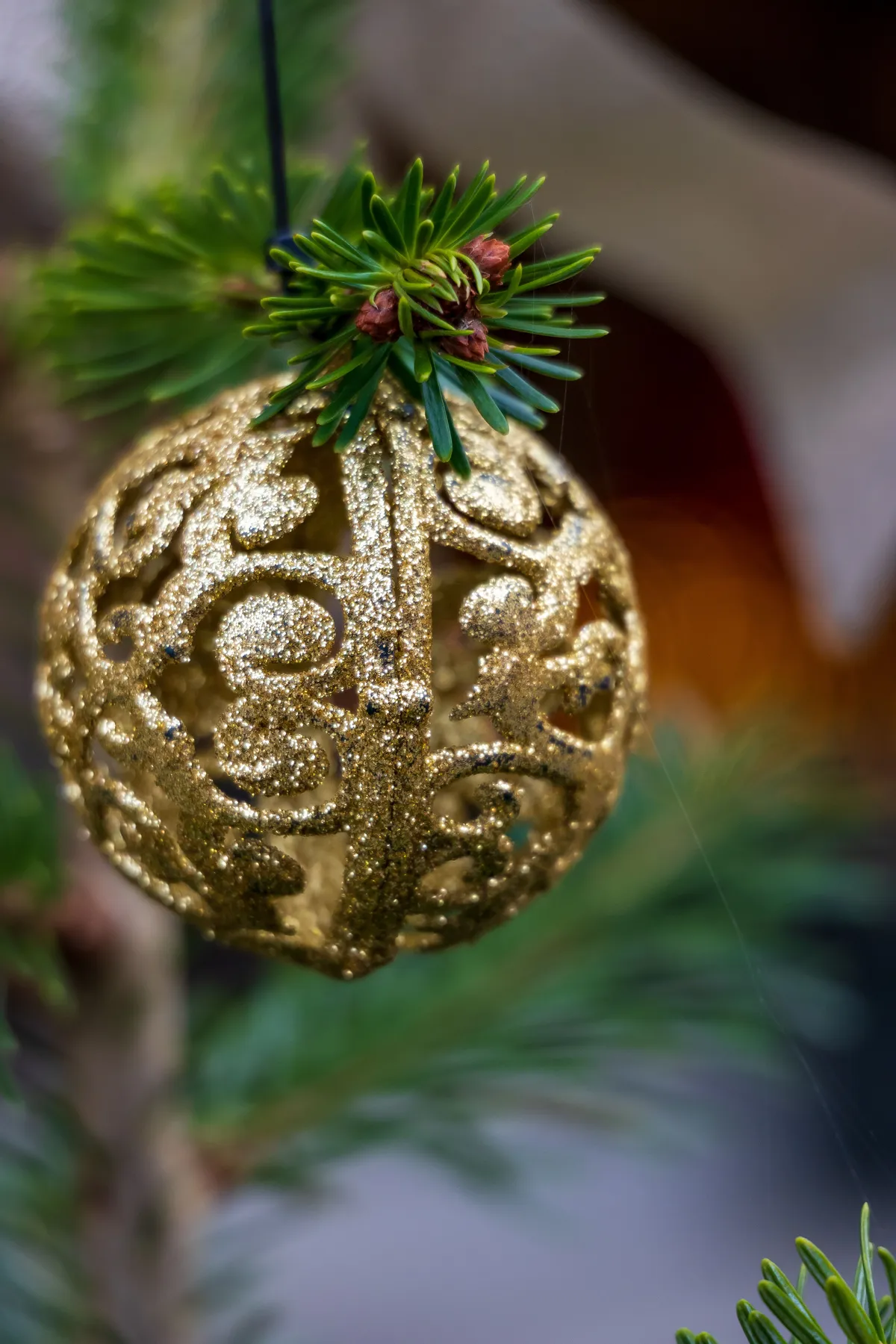 Close-up of a glittery golden Christmas ornament hanging on an evergreen branch.