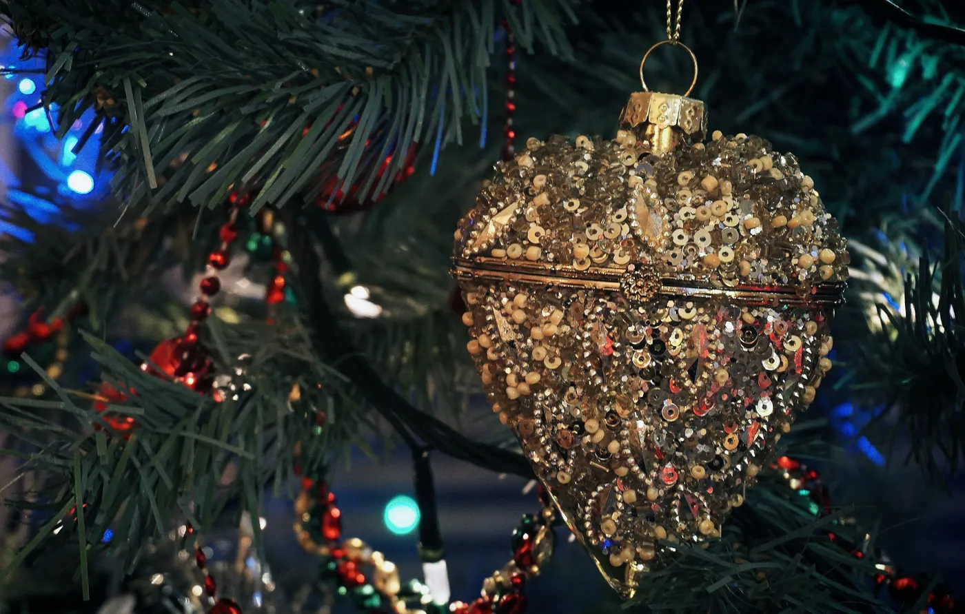 Close-up of a gold beaded ornament hanging on a decorated Christmas tree.