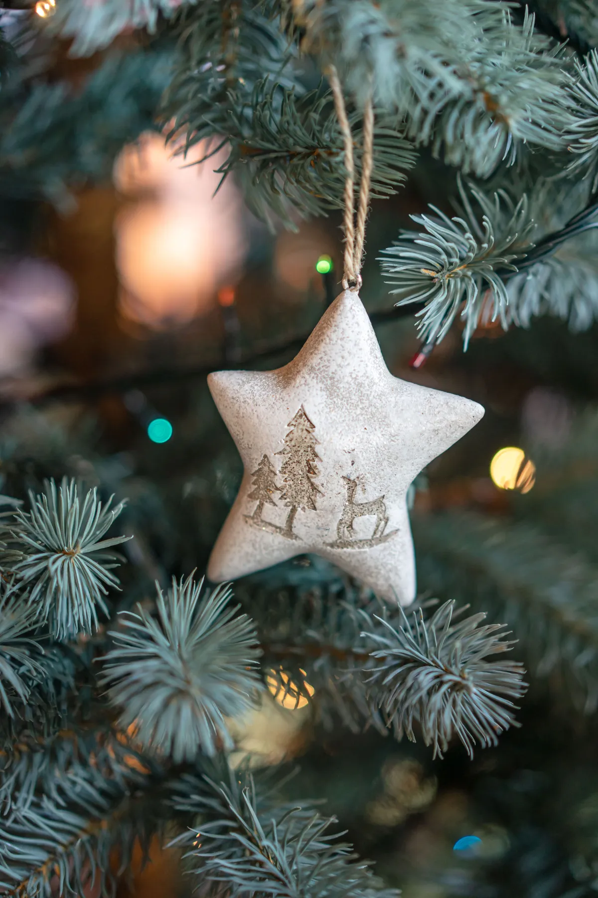 Close-up of a rustic star ornament hanging on a Christmas tree with blurred lights in the background.