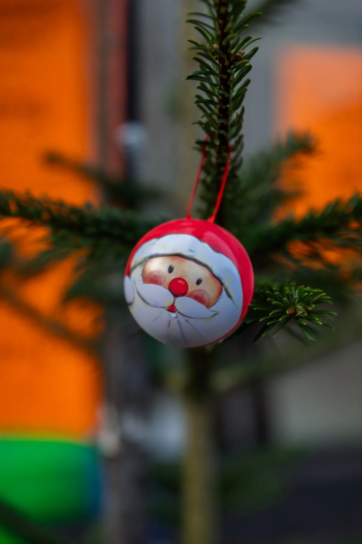Close-up of a Santa-themed ornament hanging on a Christmas tree branch outdoors.