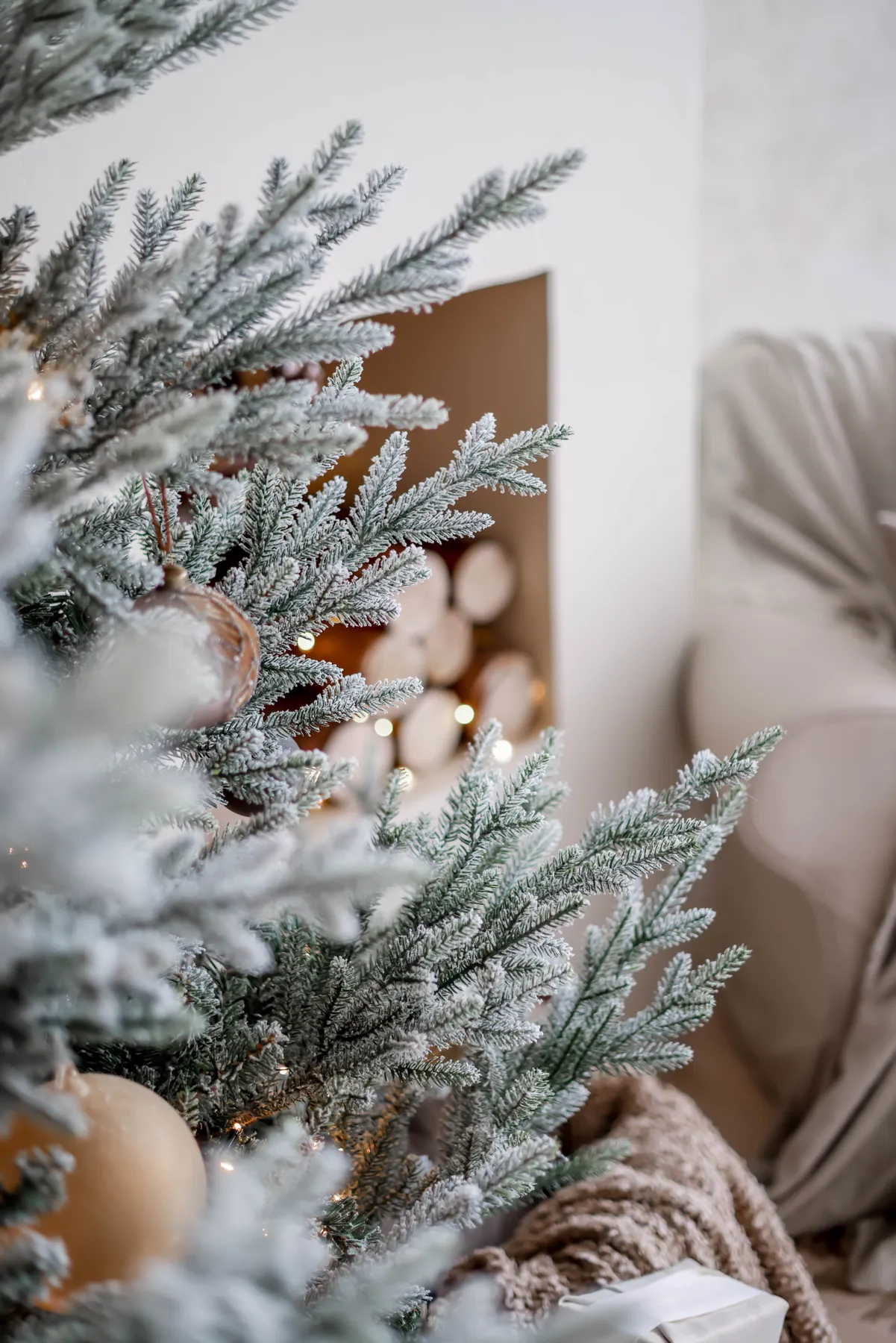 Close-up of an elegantly decorated Christmas tree with frosty needles in a cozy living room setting.