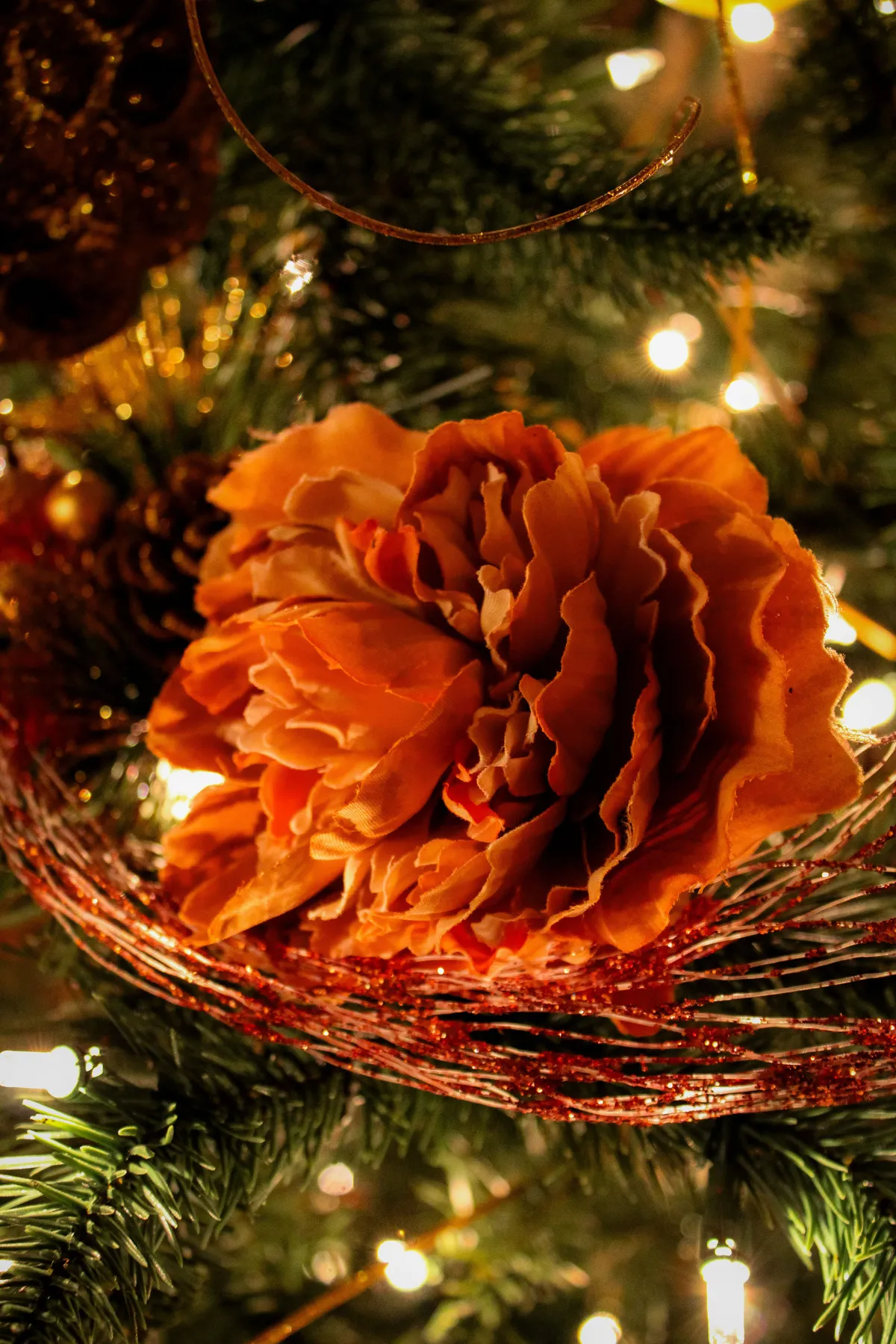 Close-up of an orange flower ornament with lights on a decorated Christmas tree, creating a warm holiday ambiance.
