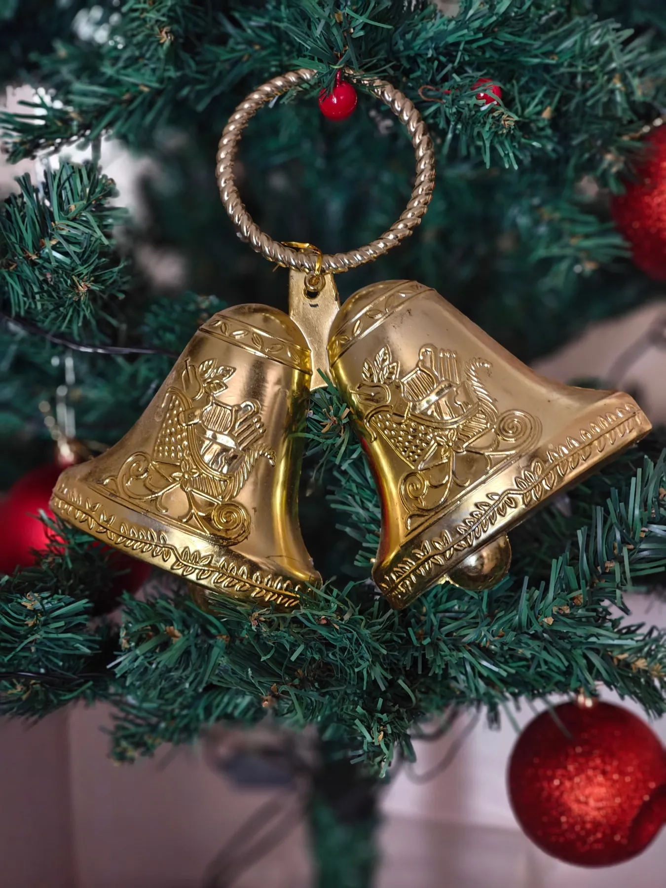 Close-up of golden bells hanging on a Christmas tree with red ornaments.