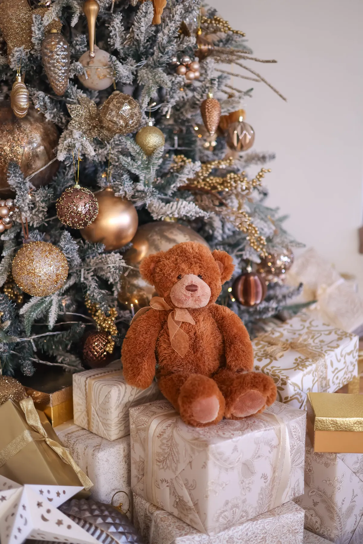 Cozy brown teddy bear sitting by a beautifully decorated Christmas tree immersed in festive holiday spirit.