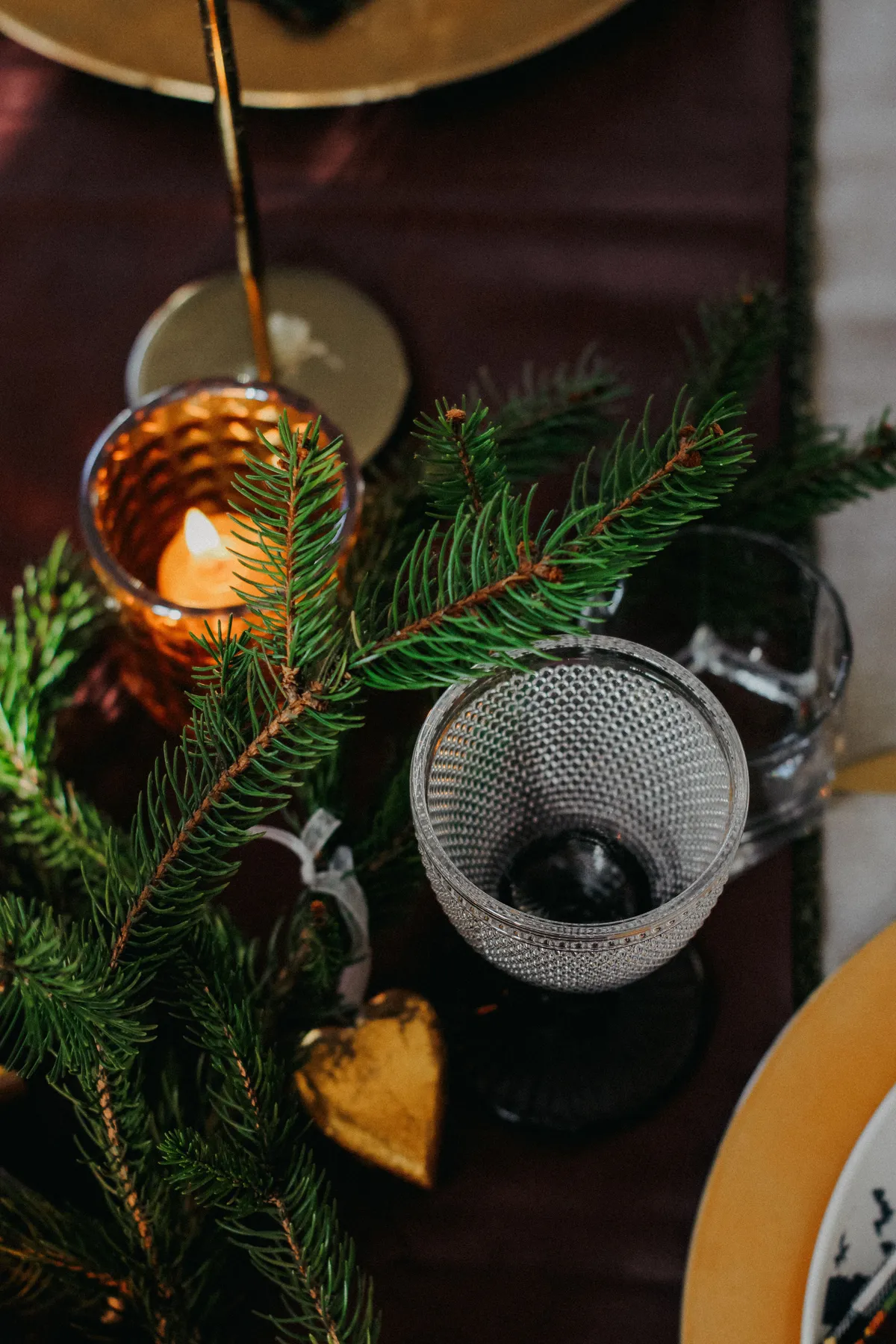 Cozy holiday table setting with pine branches, candle, and decorative elements.