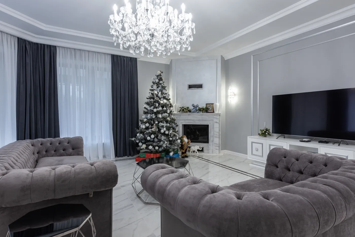 Decorated Christmas tree placed in spacious living room with comfortable sofa and armchair and modern TV set in villa