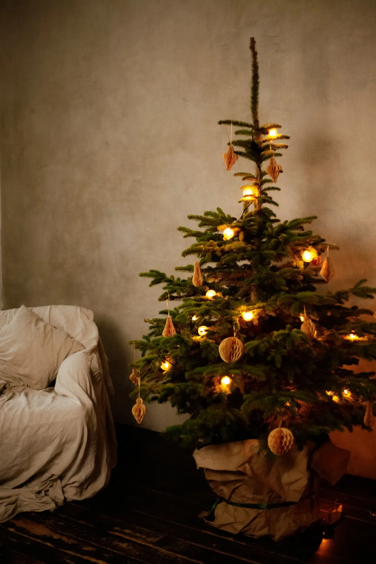 Decorated Christmas tree with warm lights beside a cozy chair indoors.