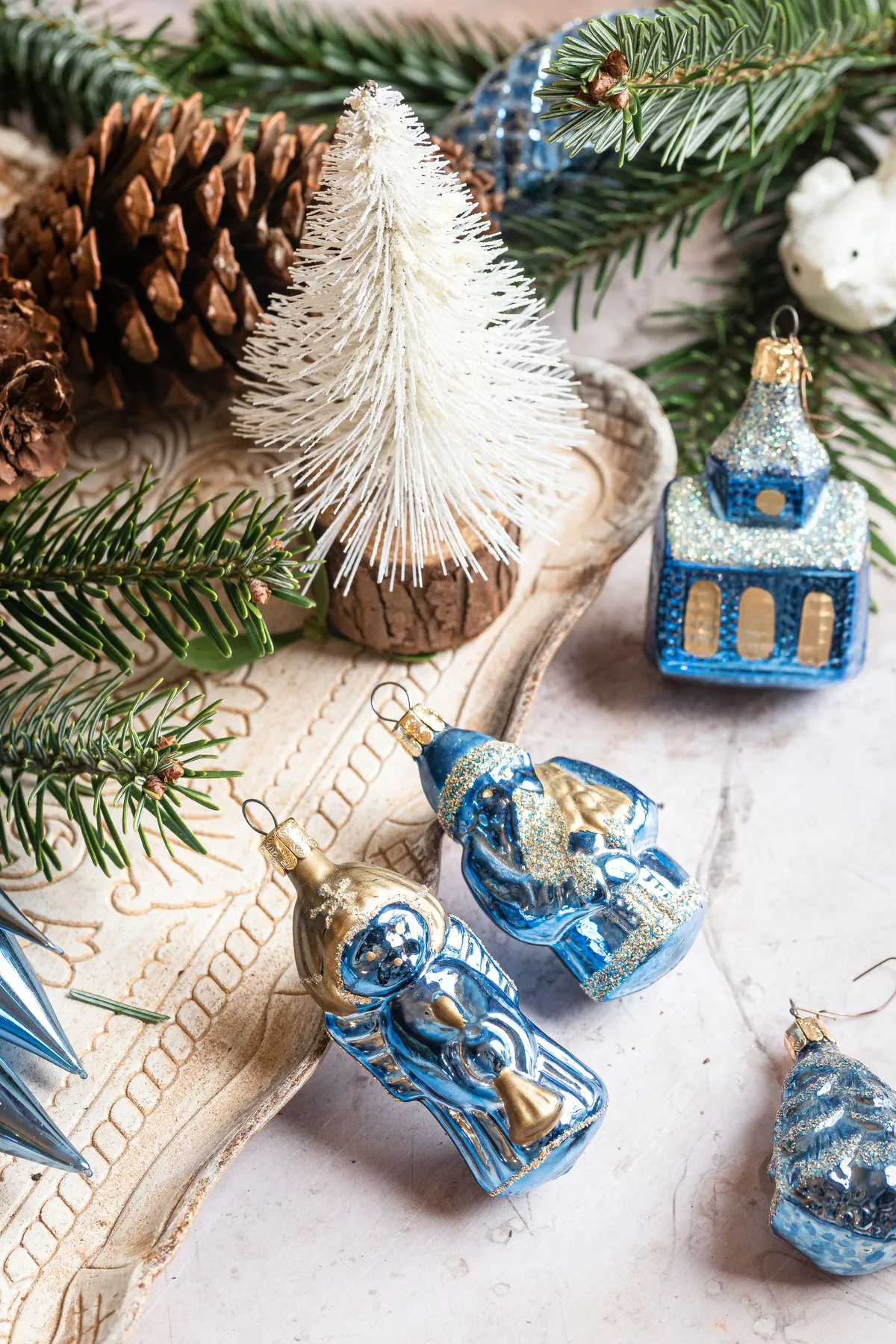 Elegant blue and silver Christmas ornaments with pine cones and a snowy tree.