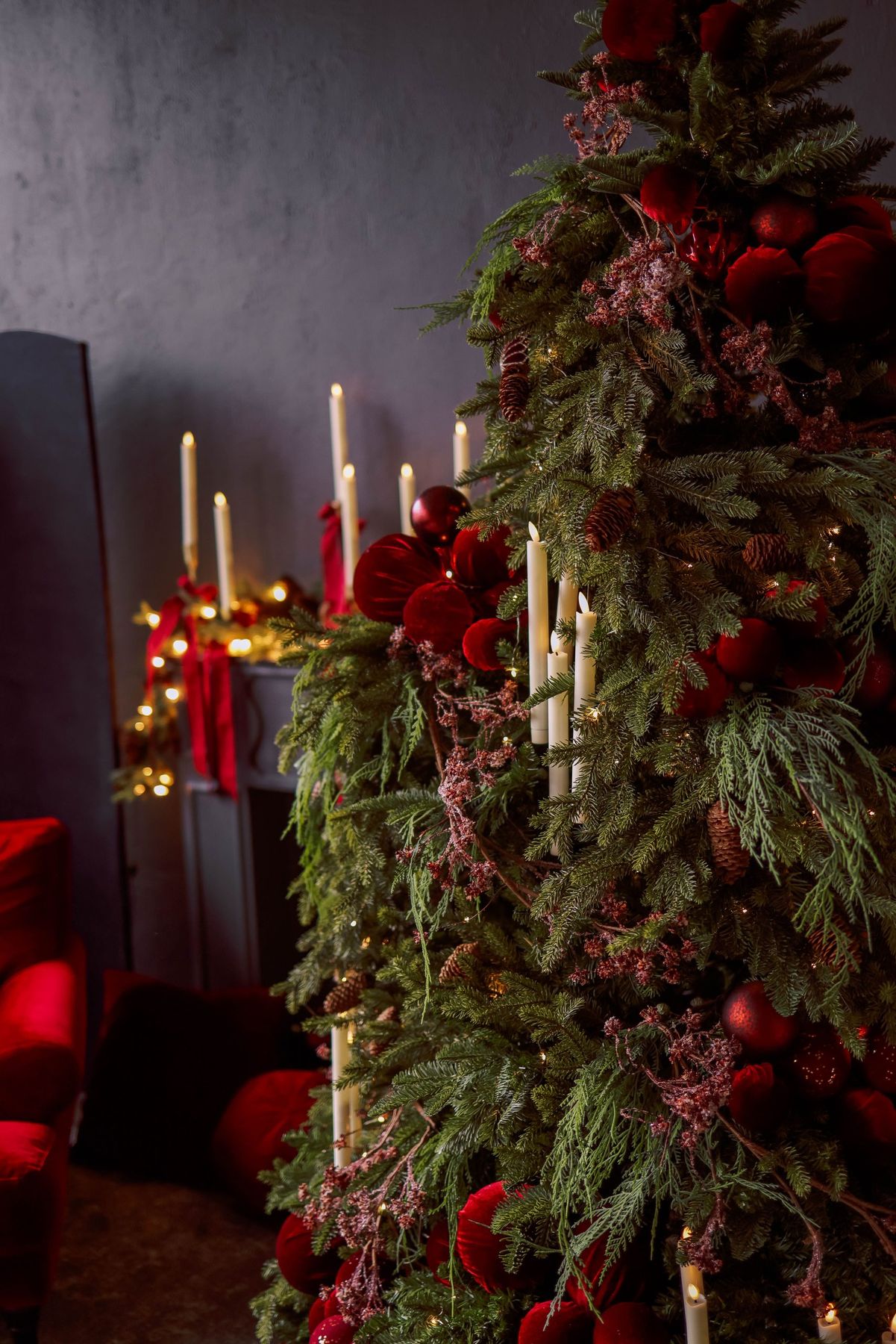 Elegant Christmas tree adorned with red ornaments and candles in a cozy room setting.
