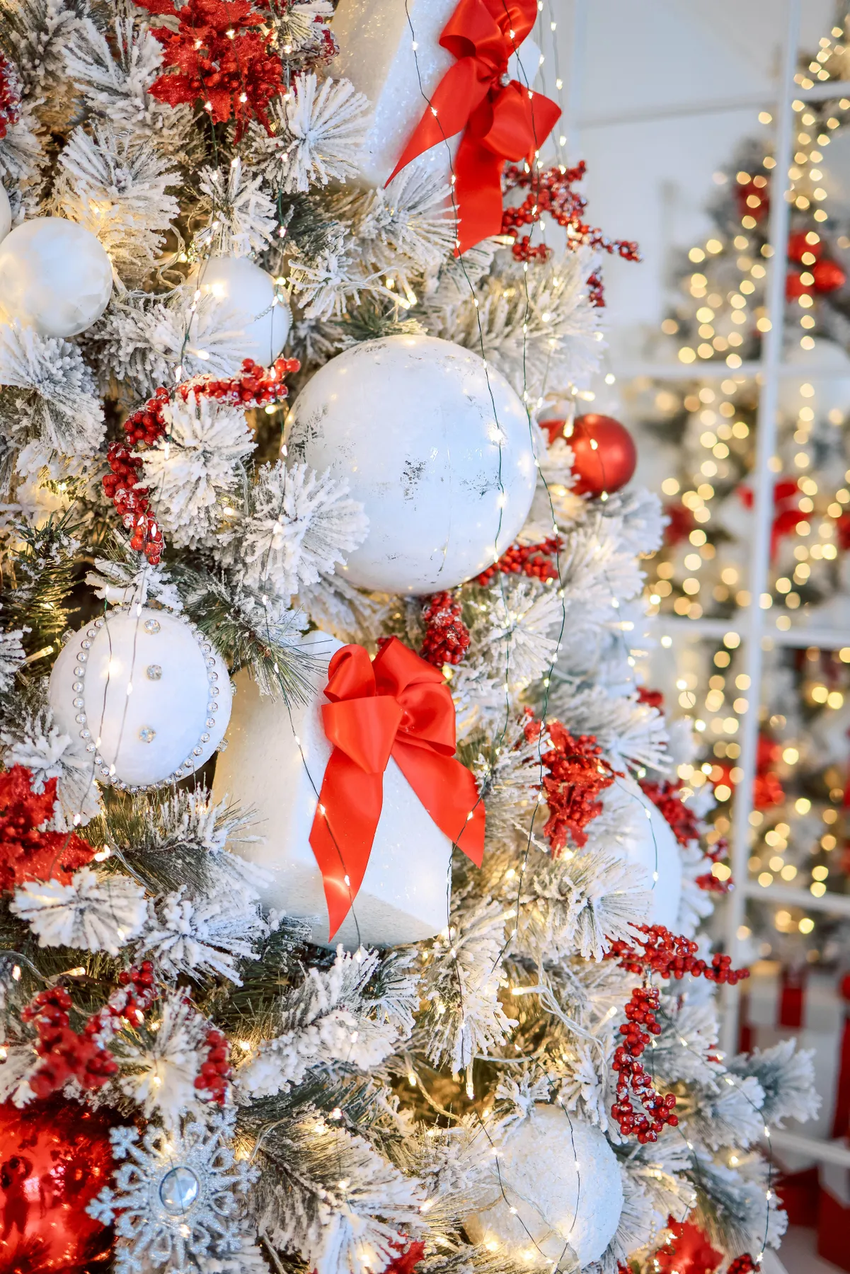 Elegant white and red themed Christmas tree with ornaments and lights indoors.