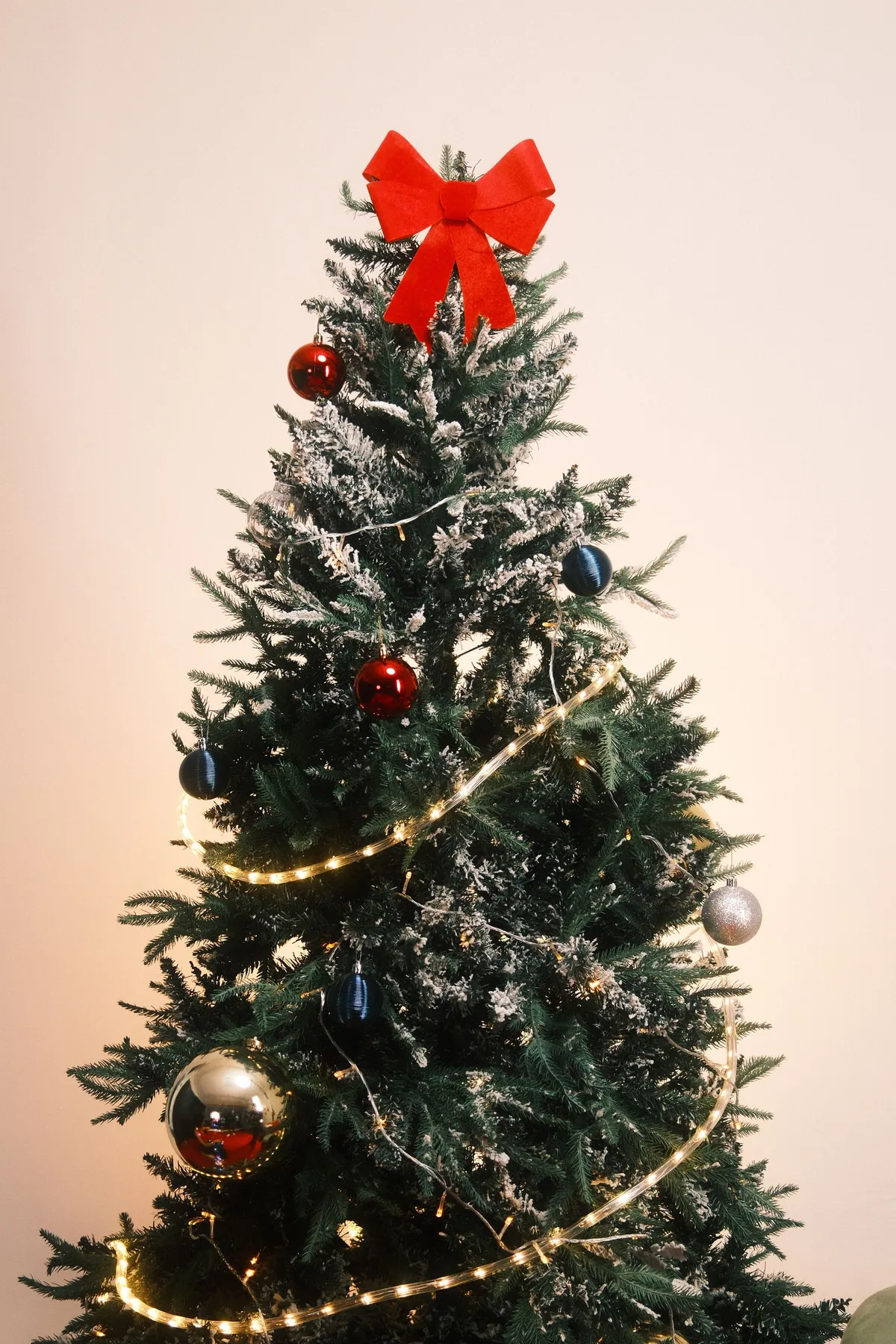 Festive Christmas tree adorned with lights, ornaments, and a striking red bow topper.