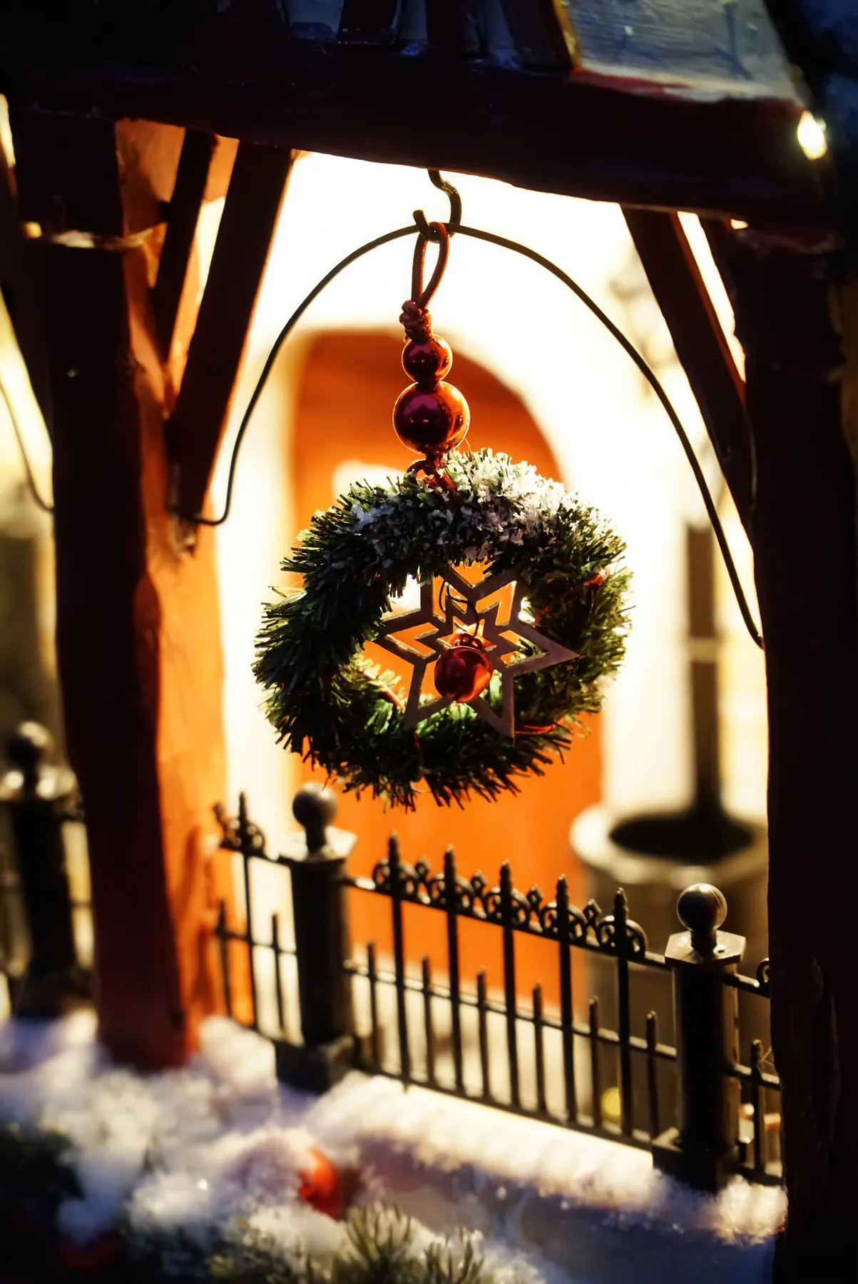 Festive Christmas wreath with snow hanging on a porch during nighttime.