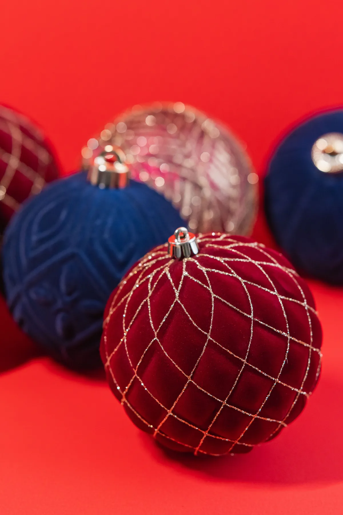 Festive holiday ornaments with vibrant colors and elegant designs against a red backdrop.