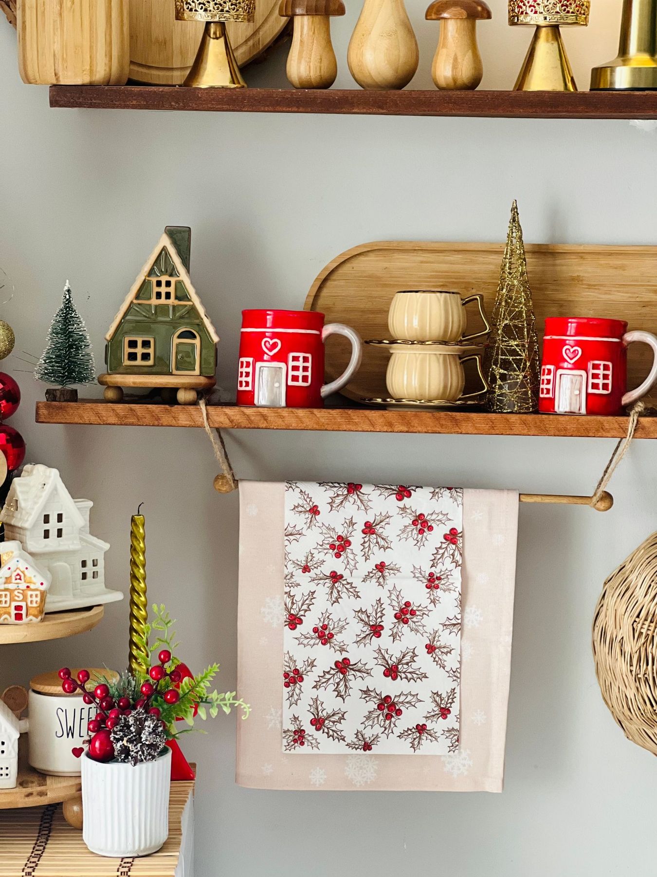 Festive kitchen shelf with Christmas-themed mugs, miniature houses, and holiday decorations.