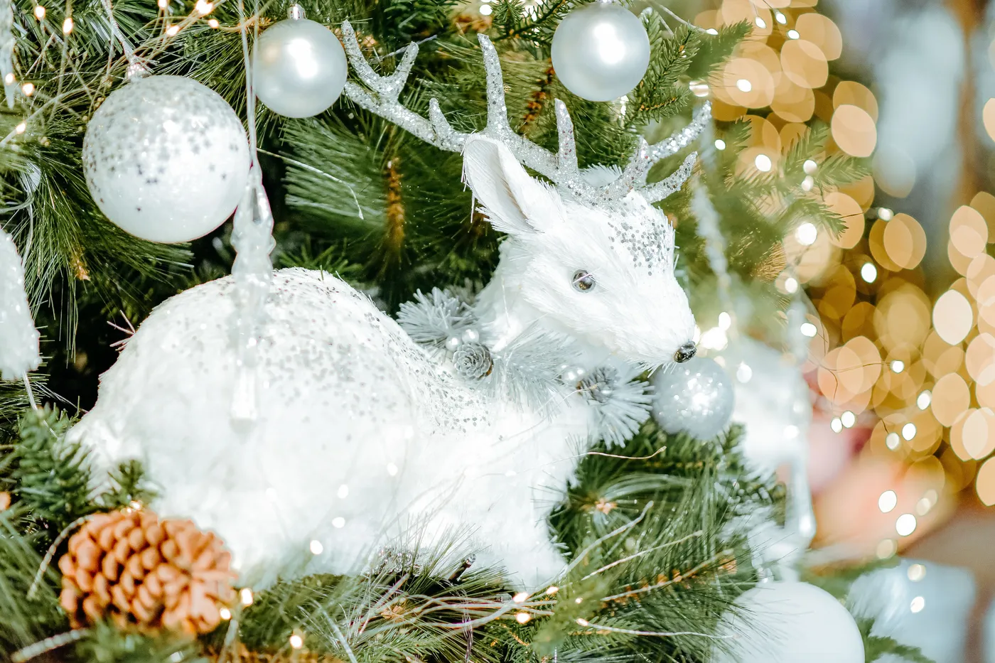 Festive white reindeer ornament on a decorated Christmas tree with glowing lights.