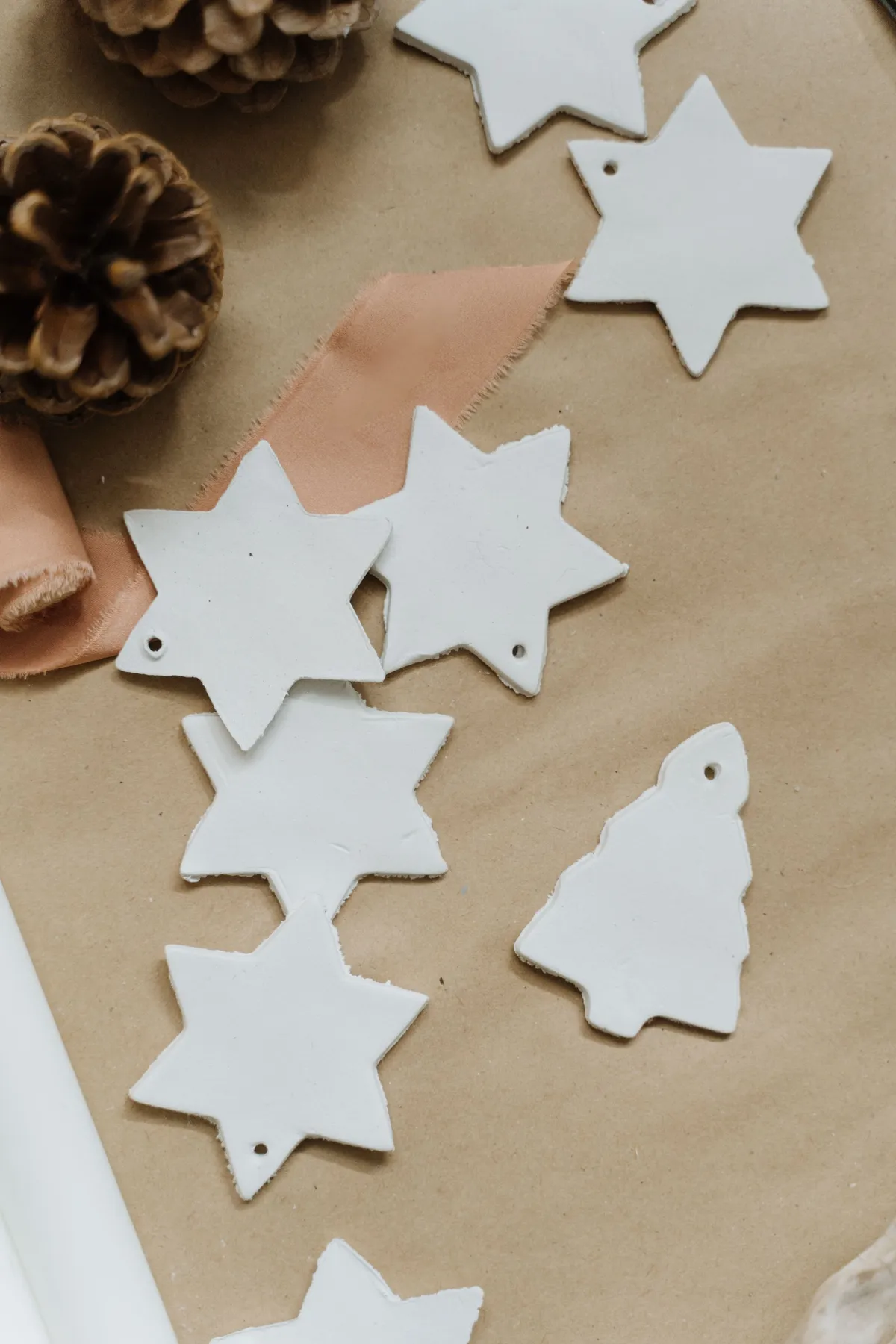 Flat lay of handmade star and tree ornaments on kraft paper with pinecones, perfect for festive crafts.