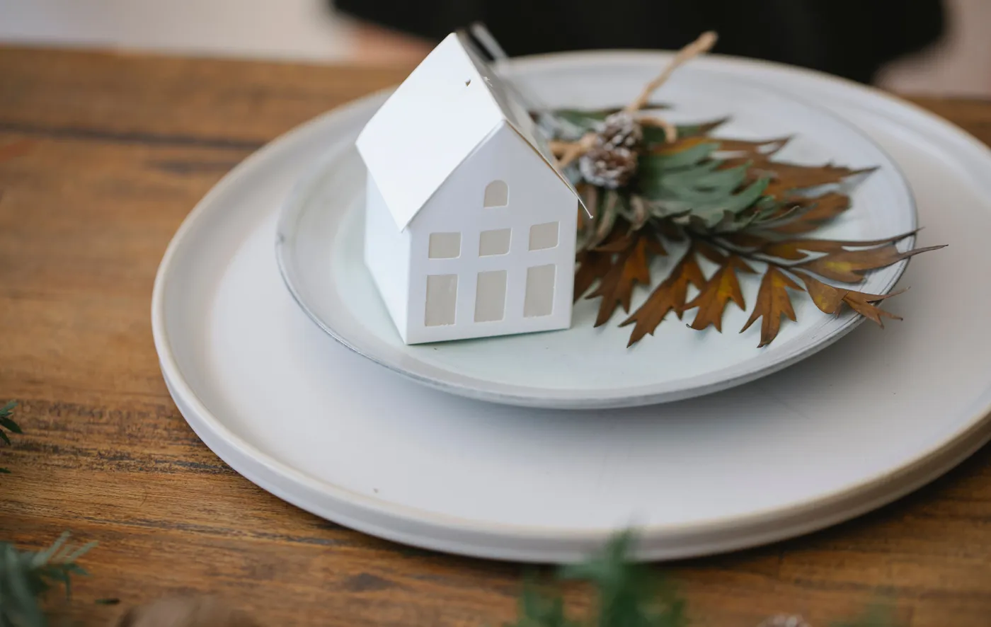 From above of round ceramic plate decorated with small Christmas leaves bouquet and handmade house placed on wooden surface