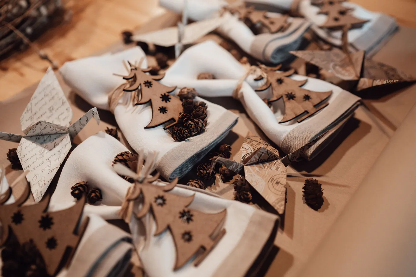 High angle of table with napkins decorated with cones and rope near small wooden Christmas trees and near origami cranes from paper in light studio