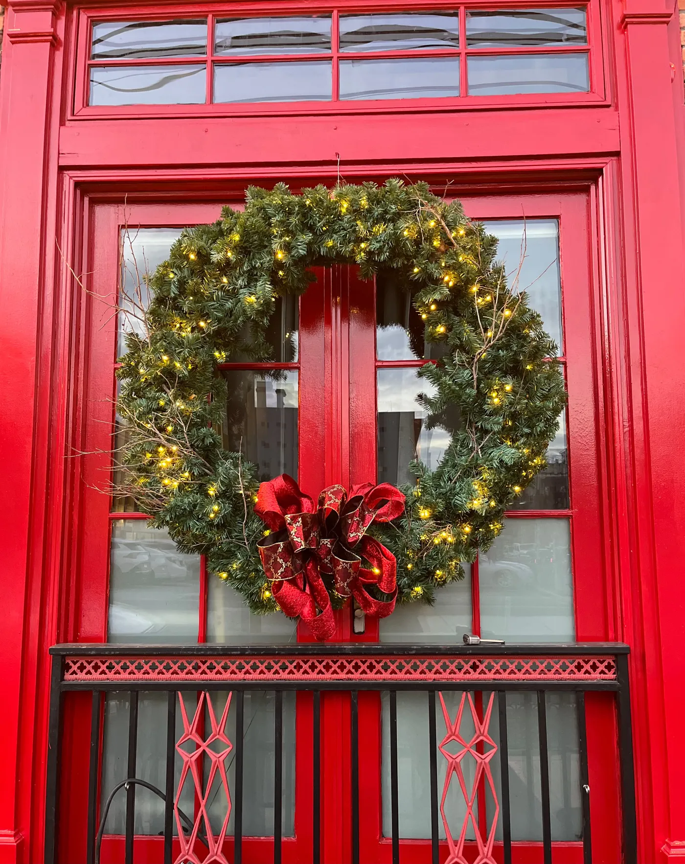 Large Christmas wreath with lights and bow on a vibrant red door in New Jersey.