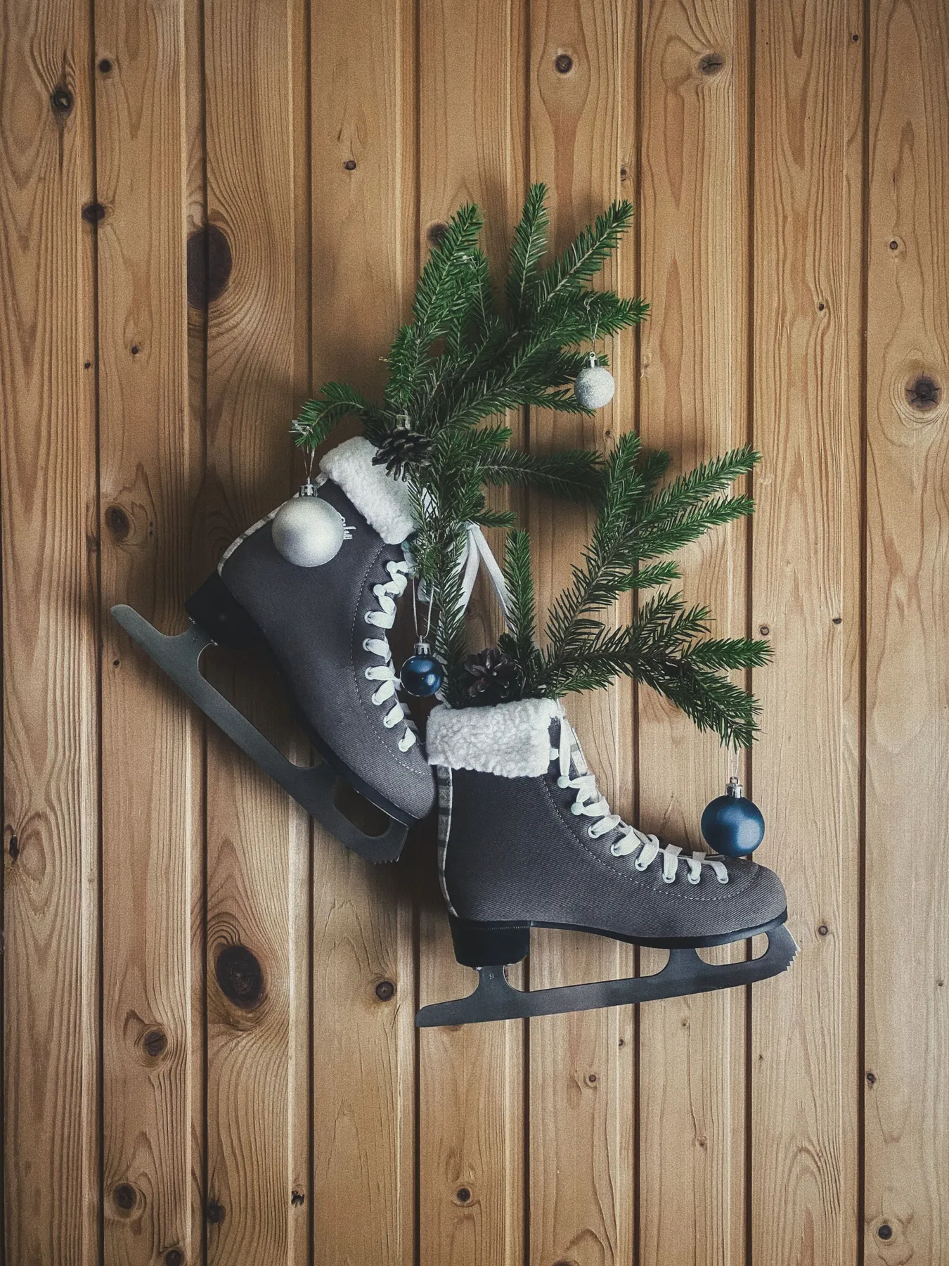 Old ice skates decorated with Christmas greenery and ornaments against a wooden wall.
