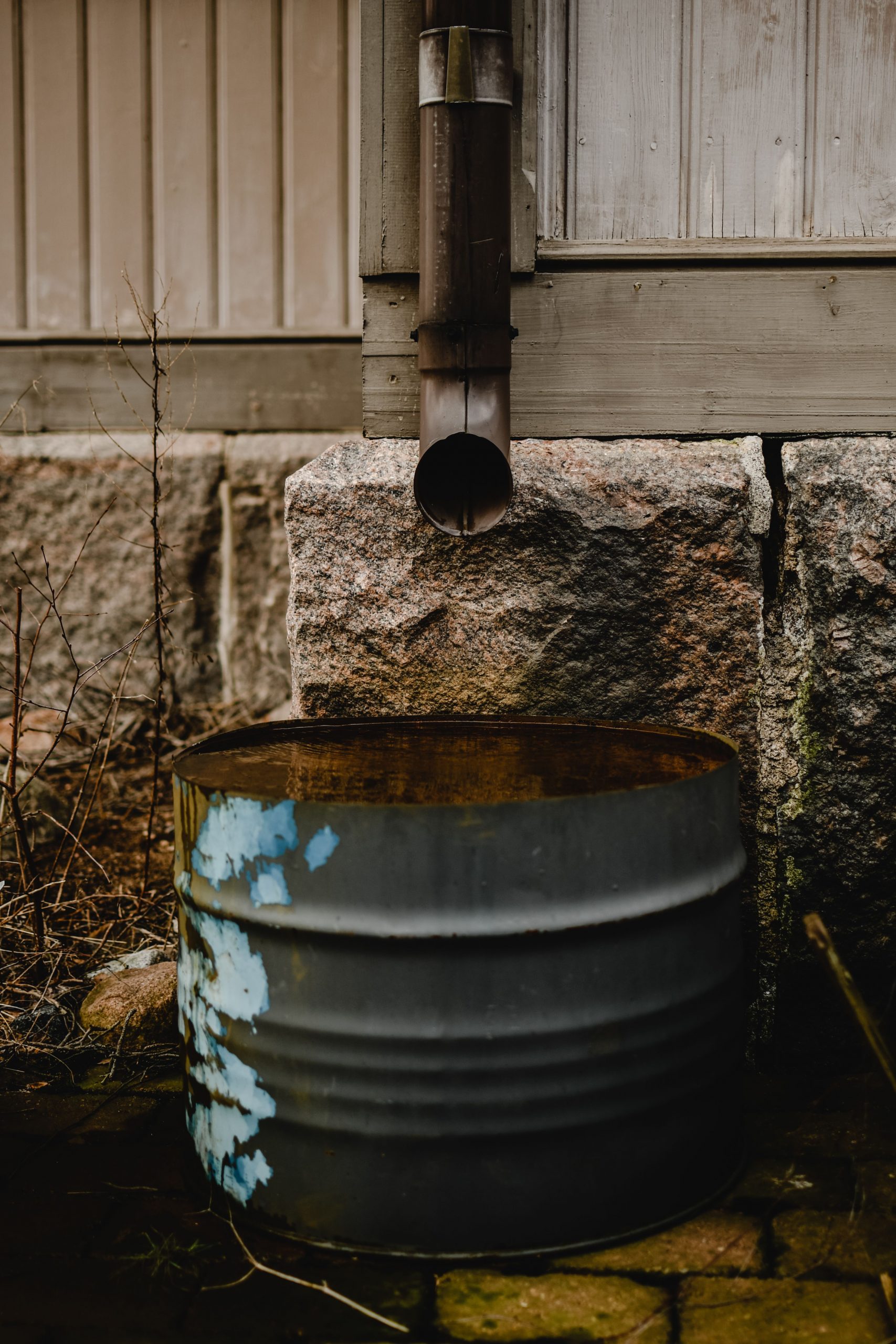 Rustic setup of a downspout and corroded barrel beside a wooden house wall in Helsinki.