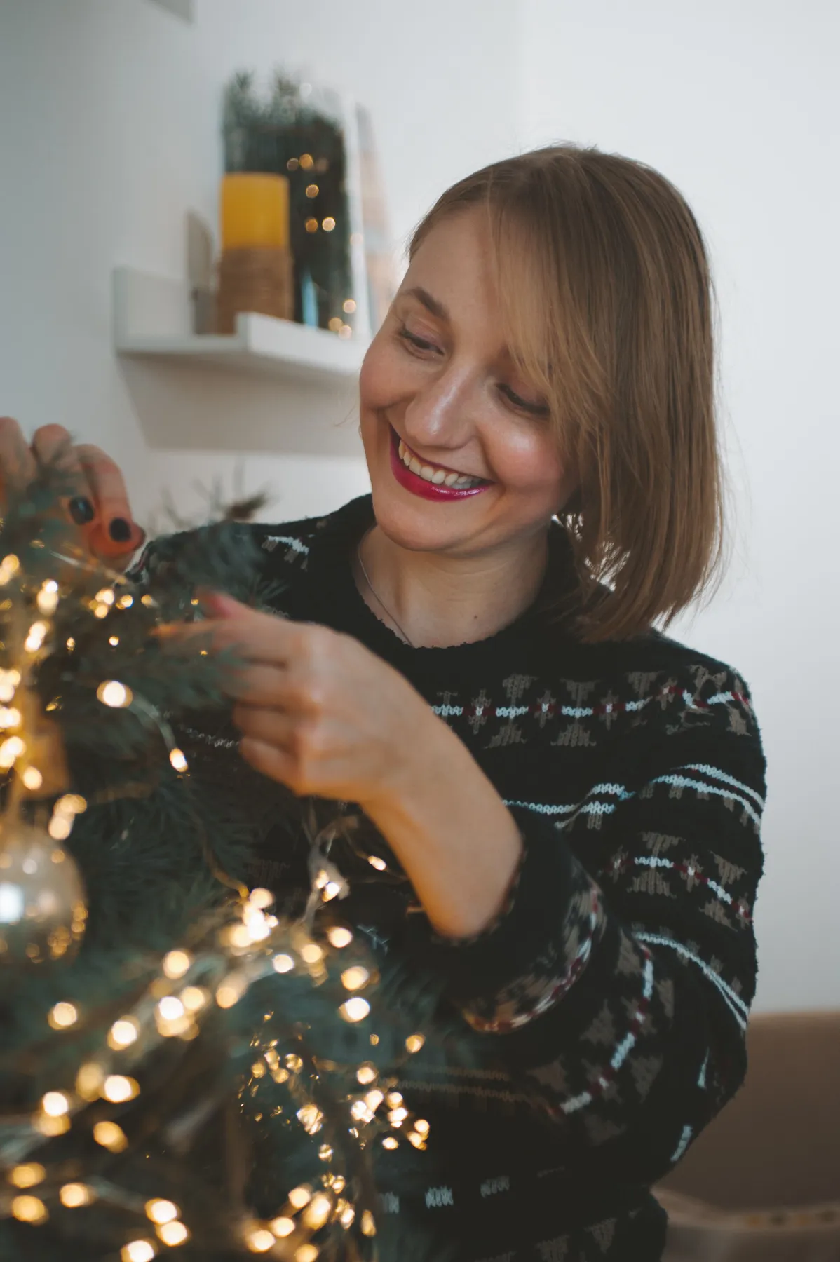 Smiling woman decorates a Christmas tree with lights, creating festive atmosphere.