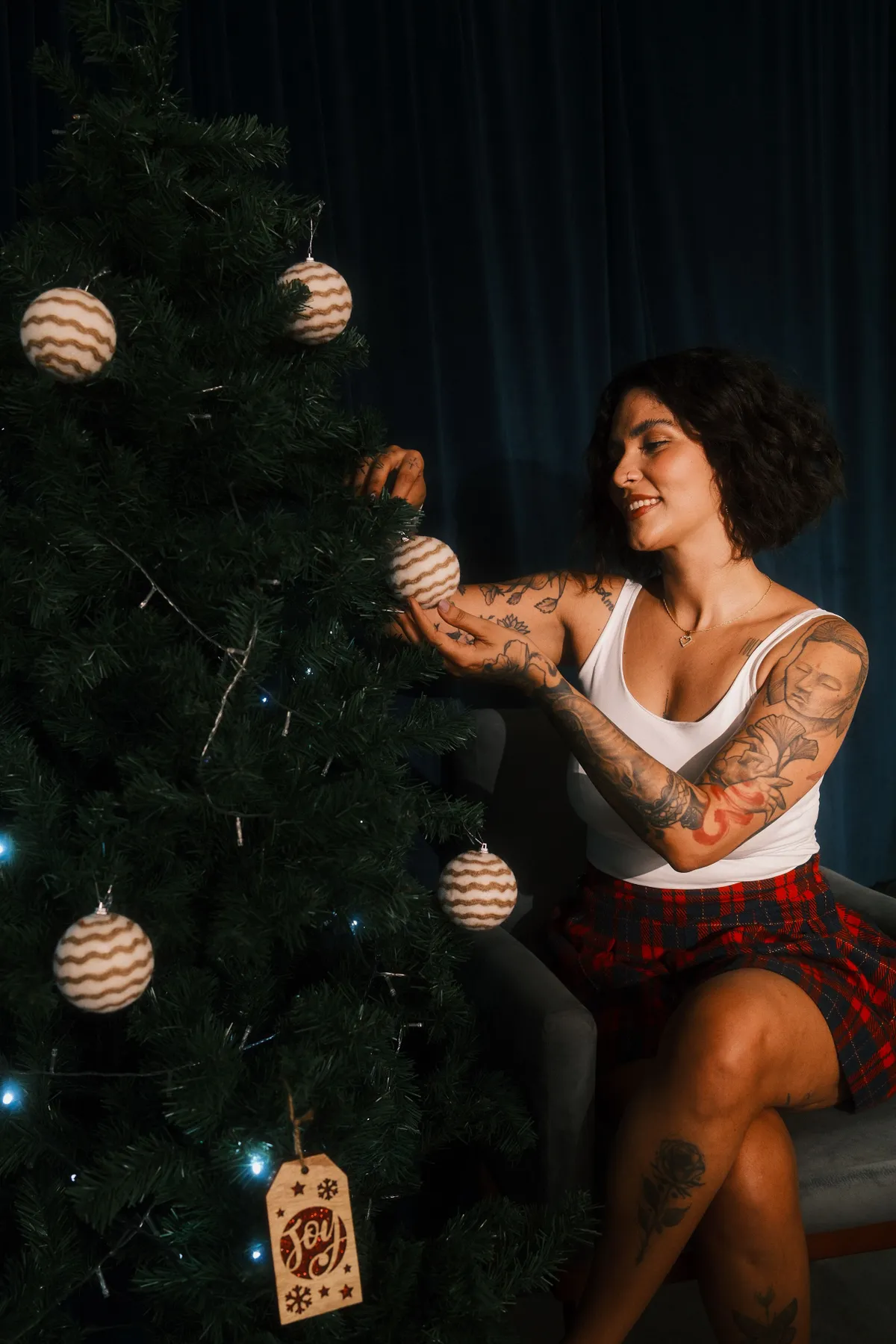 Smiling woman decorates Christmas tree, creating a cozy holiday atmosphere indoors.
