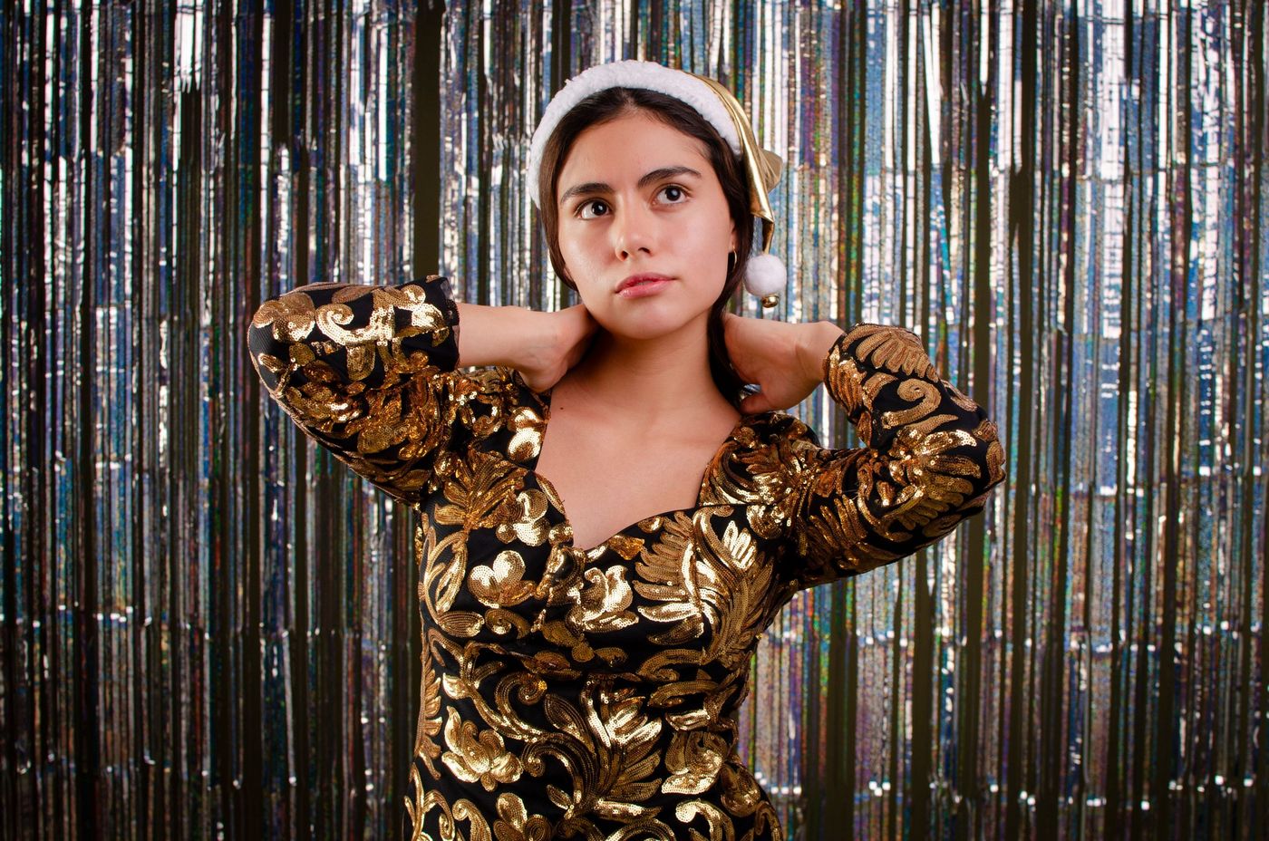 Sophisticated holiday portrait of a woman in a gold dress and Santa hat, ready for celebration.