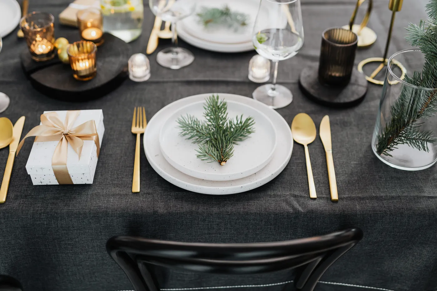 Sophisticated holiday table setting with pine decor and golden utensils, perfect for Christmas gatherings.