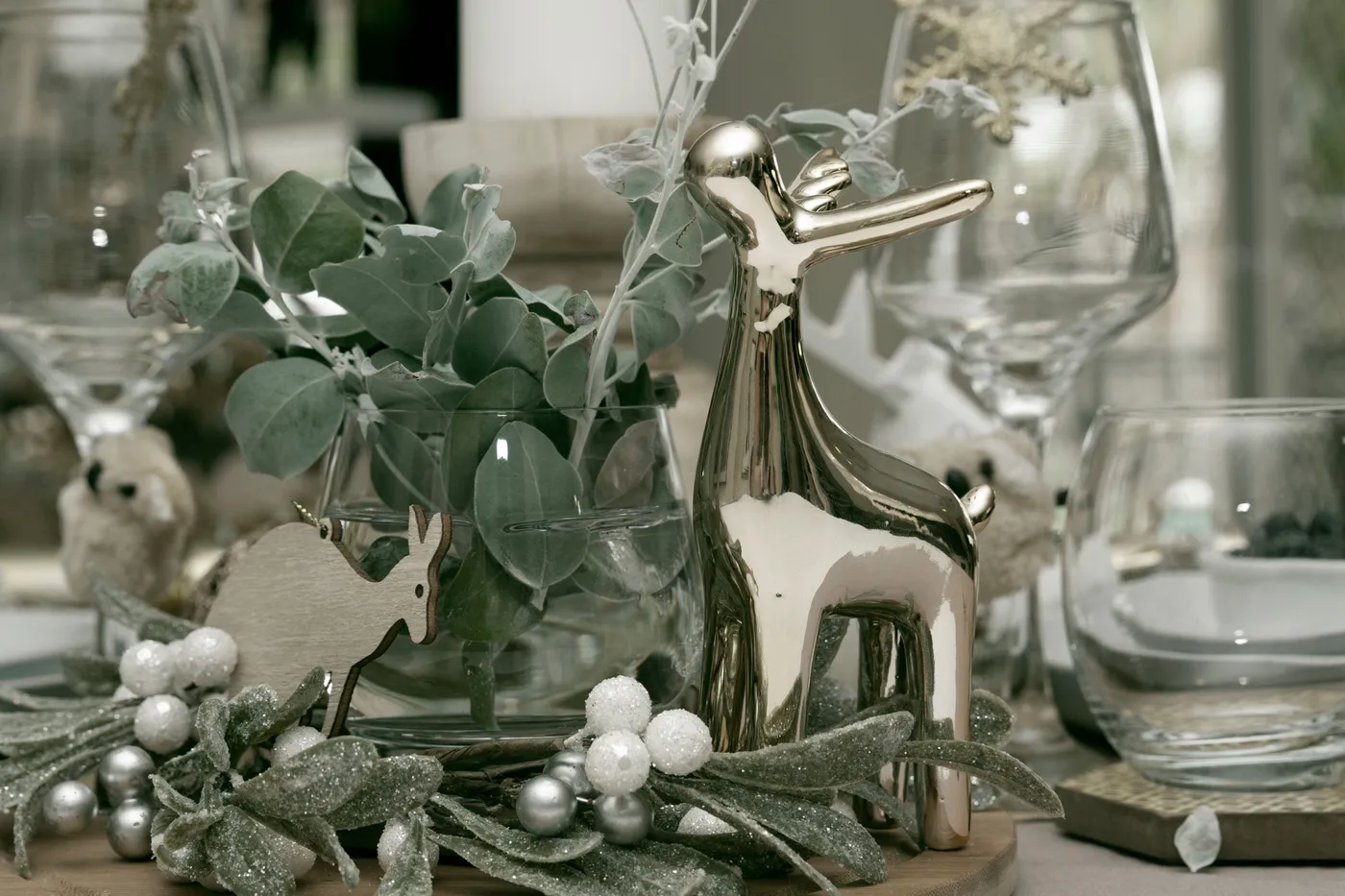 Stylish winter table setting featuring a metallic deer figurine and greenery.