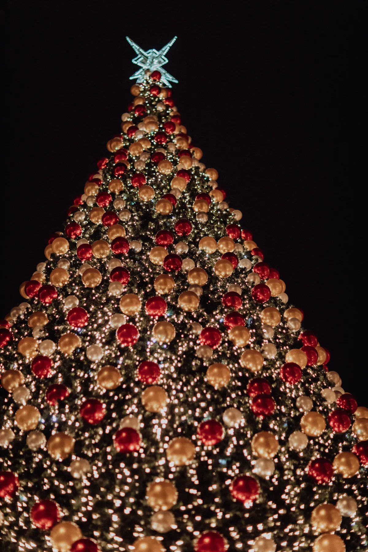 Vertical shot of a sparkling Christmas tree with colorful ornaments and lights against a dark night sky.