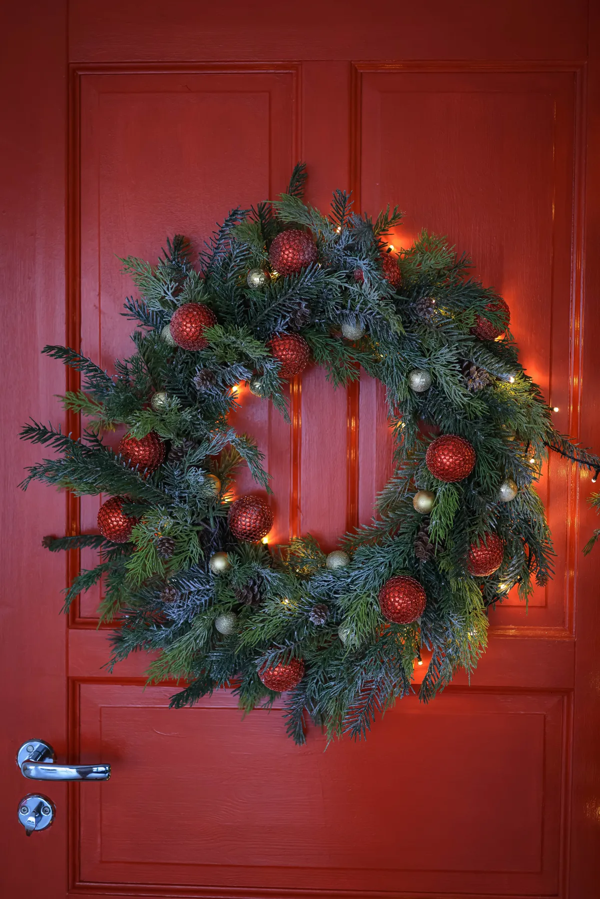 Vibrant Christmas wreath with baubles and lights adorning a red door.