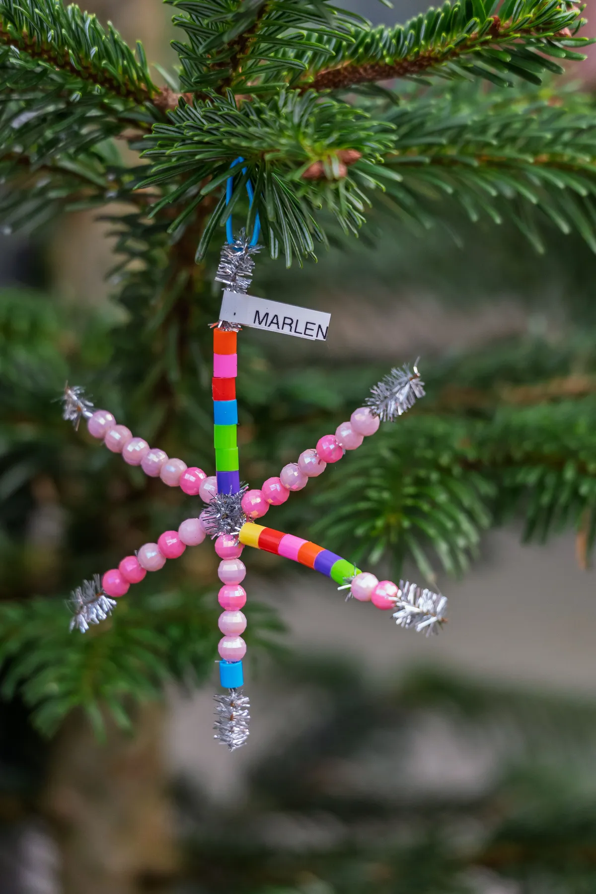 Vibrant handmade beaded snowflake ornament on Christmas tree branch.