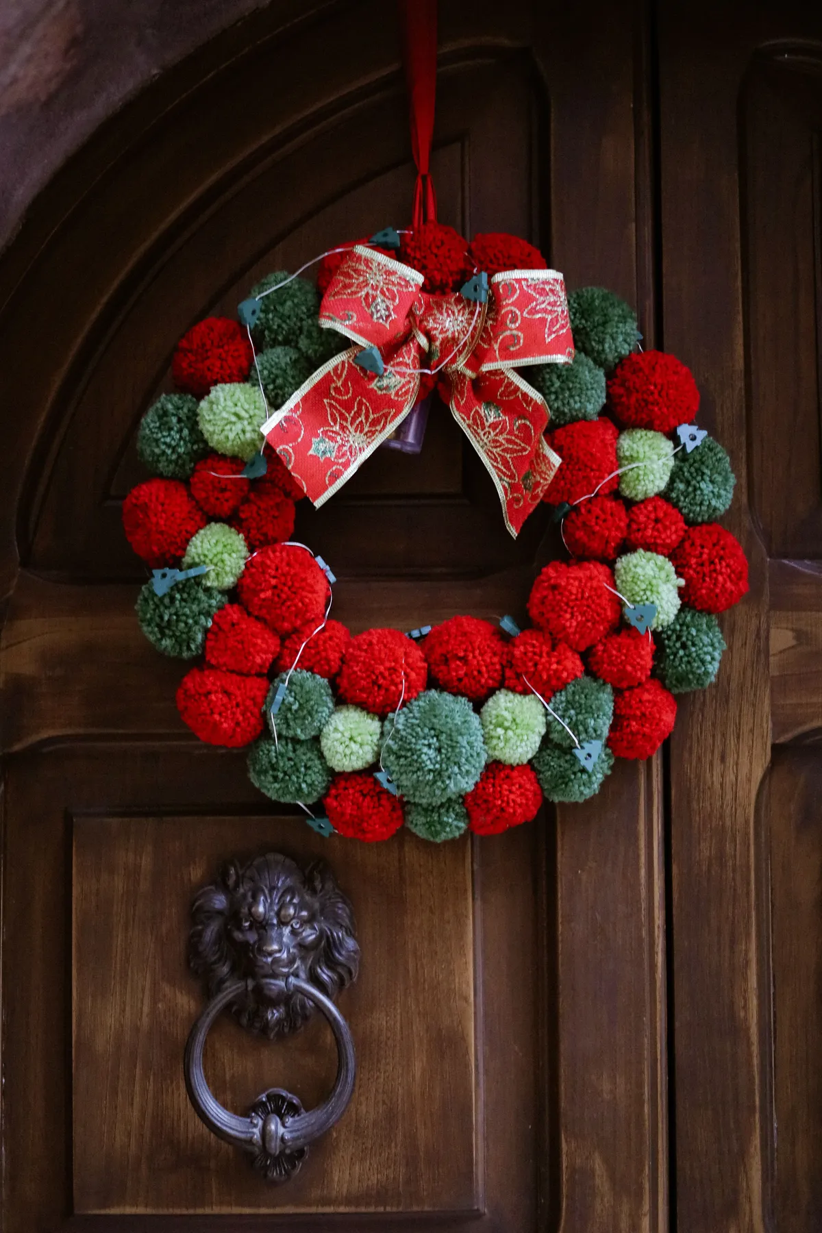 Vibrant red and green Christmas wreath with bow decorates a wooden door.