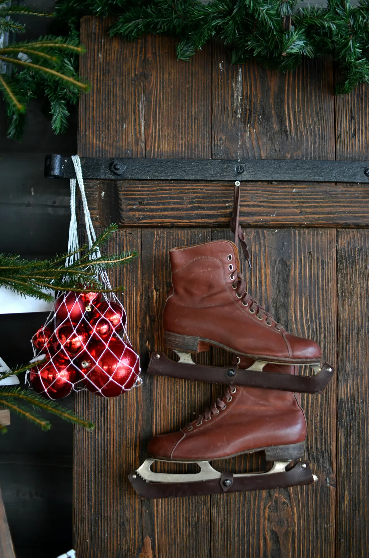 Vintage ice skates hang on a wooden door with ornaments