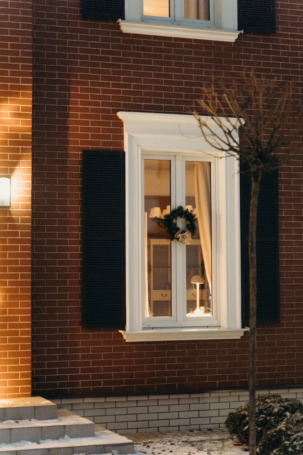 Warm exterior view of a brick house window adorned with a decorative wreath.