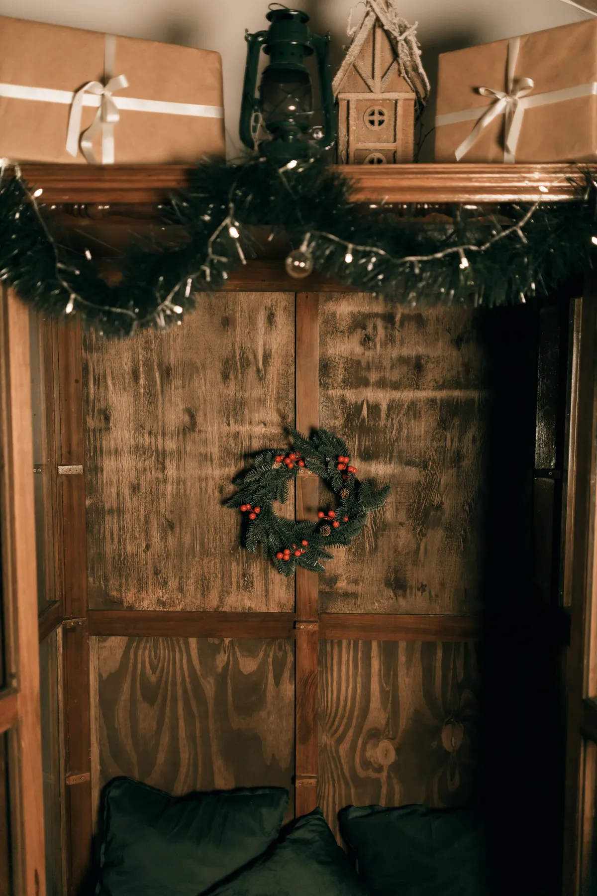 Warm wooden corner decorated for Christmas with a wreath, garland, and gift boxes.